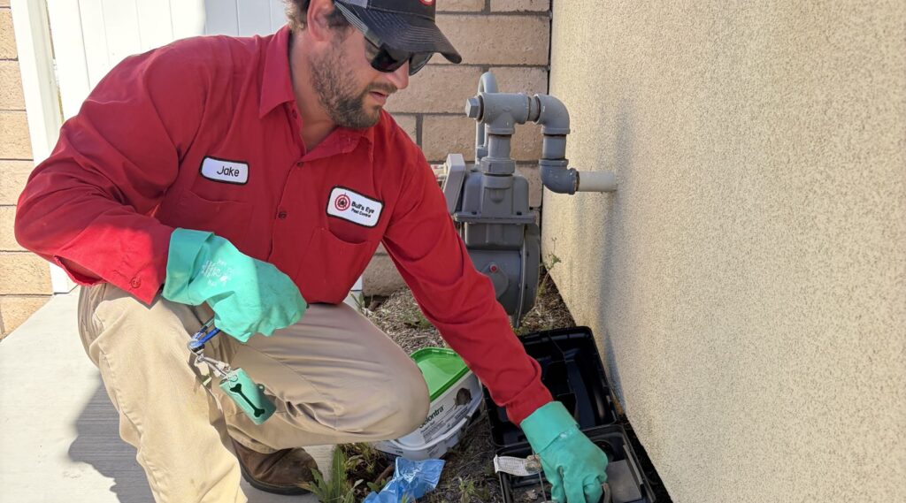 Bull's Eye Pest Control technician servicing a rodent bait station along the exterior of a Southern California home