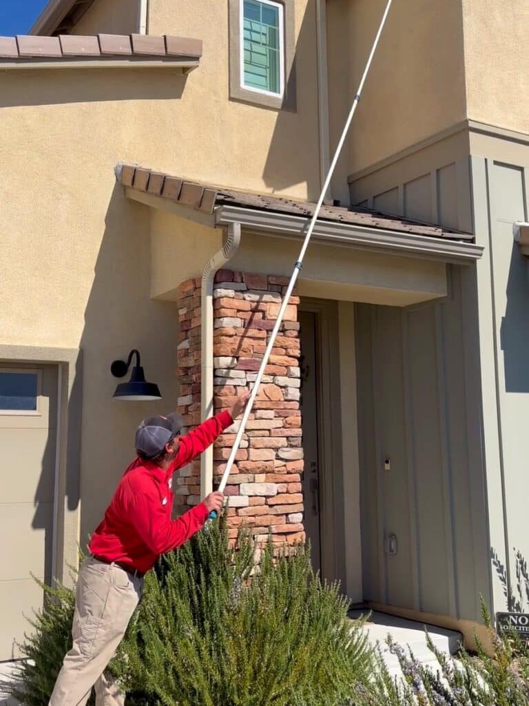 Bull's Eye technician clearing spider webs from the eaves of a two-story Lake Elsinore home